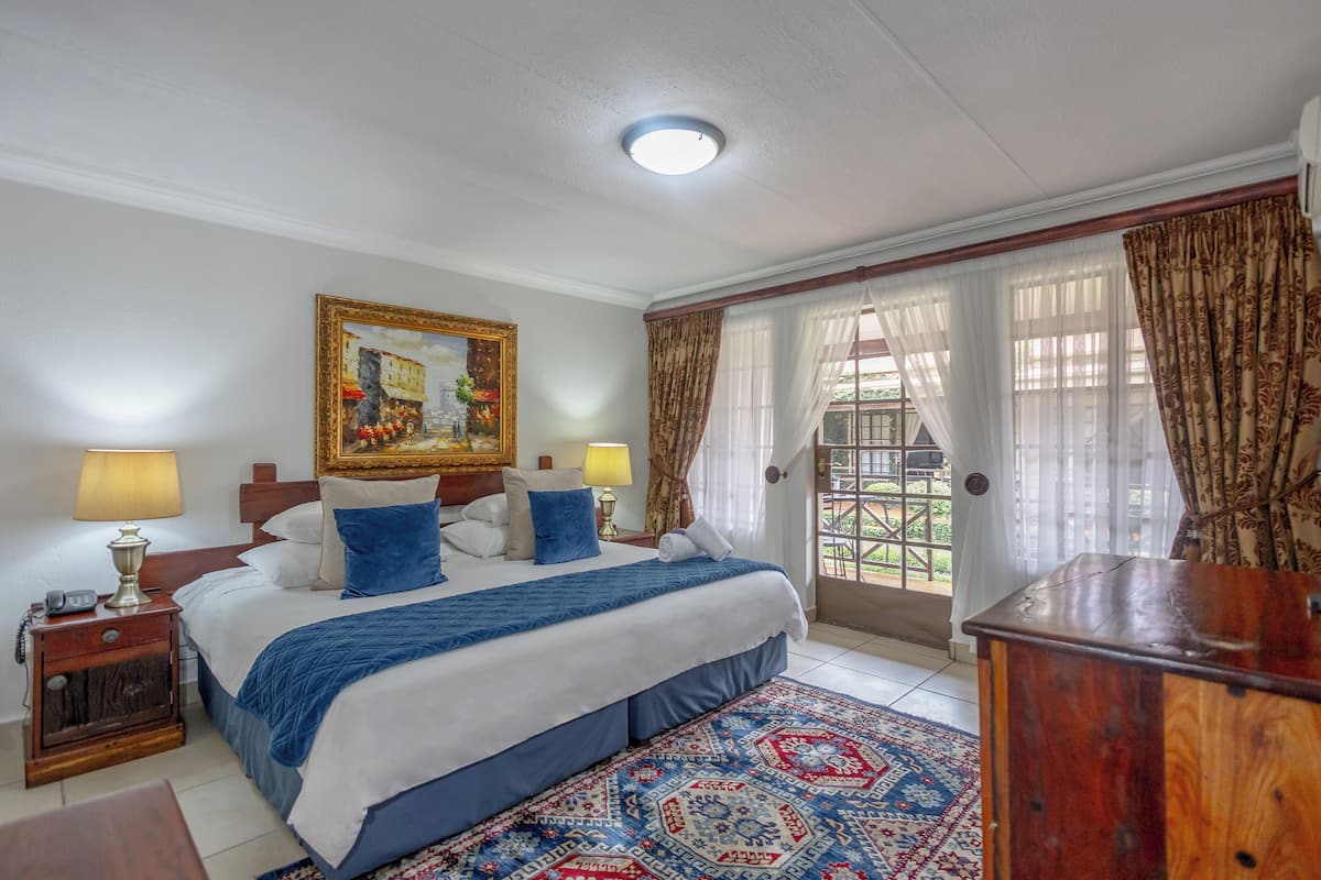 A well-lit bedroom with a large bed, a painting above the bed, and a view through the window.