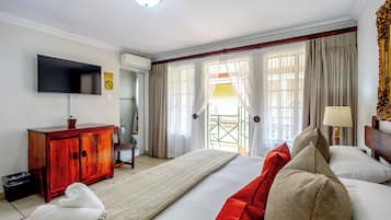 Habitación de hotel con una cama grande, un televisor montado en la pared, un armario de madera y una ventana con cortinas.