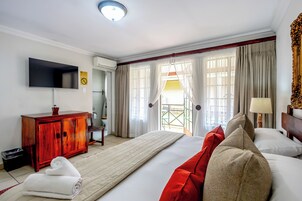 Habitación de hotel con una cama grande, un televisor montado en la pared, un armario de madera y una ventana con cortinas.