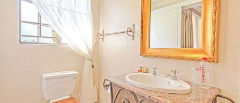 Baño con inodoro, lavamanos, espejo y ventana con cortinas.