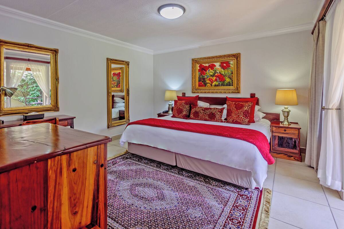A hotel room with a large bed, two bedside tables, a wooden desk, a patterned rug, and two framed pictures on the wall.