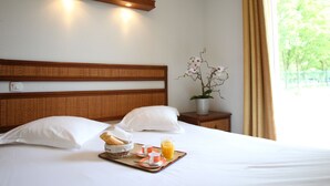 A neatly made bed with a tray of breakfast items, a bedside table with a potted plant, and a window with curtains.