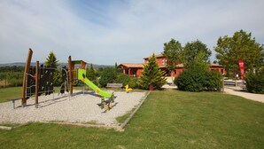 A playground with a green slide and climbing structures, surrounded by a grassy area and trees.