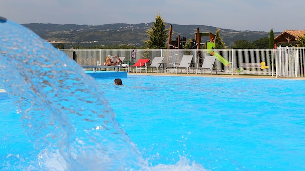 A swimming pool with a person swimming, a water slide, and a fenced area with lounge chairs.