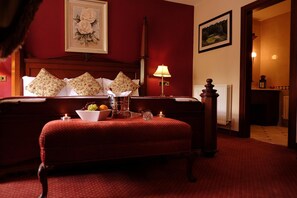 A hotel room with a large bed, a bedside table with a lamp, a red carpeted floor, and a framed picture on the wall.