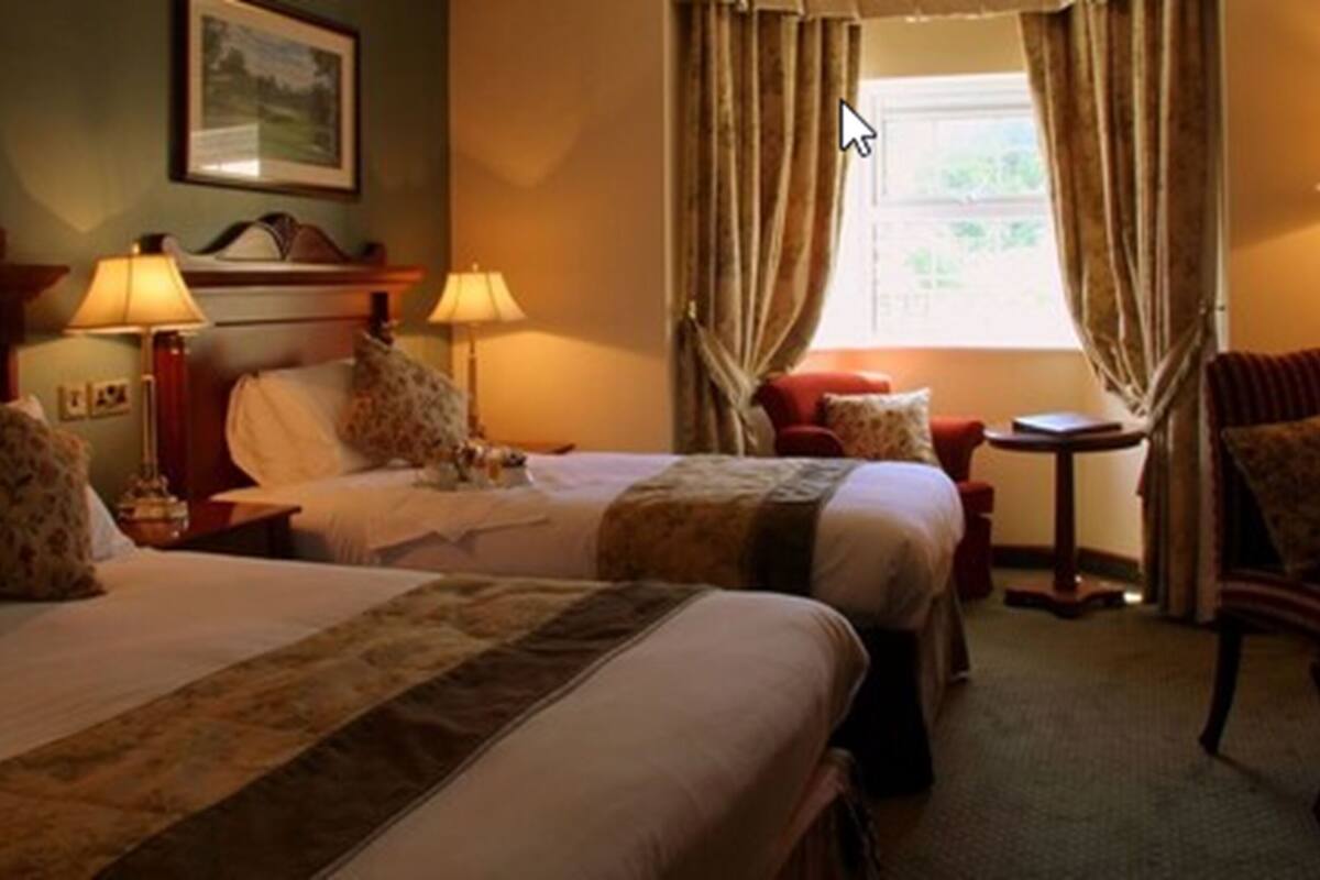 Habitación de hotel con dos camas, un escritorio y una silla. Hay dos lámparas en las mesitas de noche.
