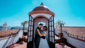 A couple embracing in a gazebo on a rooftop with a clear sky and cityscape in the background.