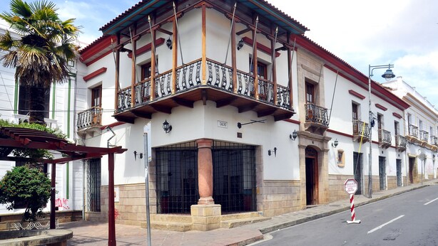 A traditional building with a balcony, a large door, and a street sign.