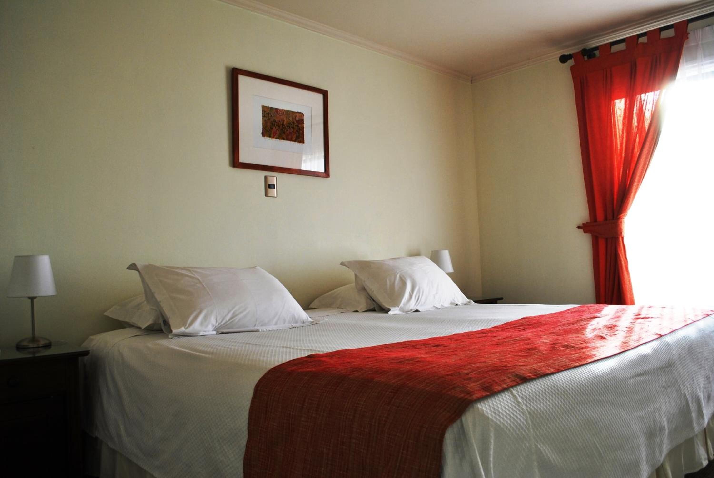 Una habitación de hotel con una cama, una mesita de noche, una lámpara, un cuadro en la pared y una cortina roja.