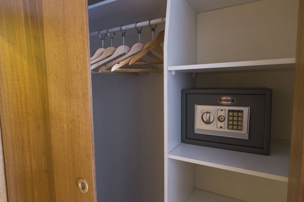 A wooden door leading to a closet with a hanging rack and a safe on a shelf.
