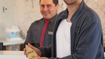 A man holding a numbered envelope in a hotel lobby with wooden paneling and hanging light fixtures.