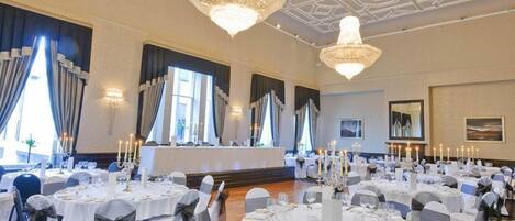 A banquet hall with round tables, chandeliers, and large windows.