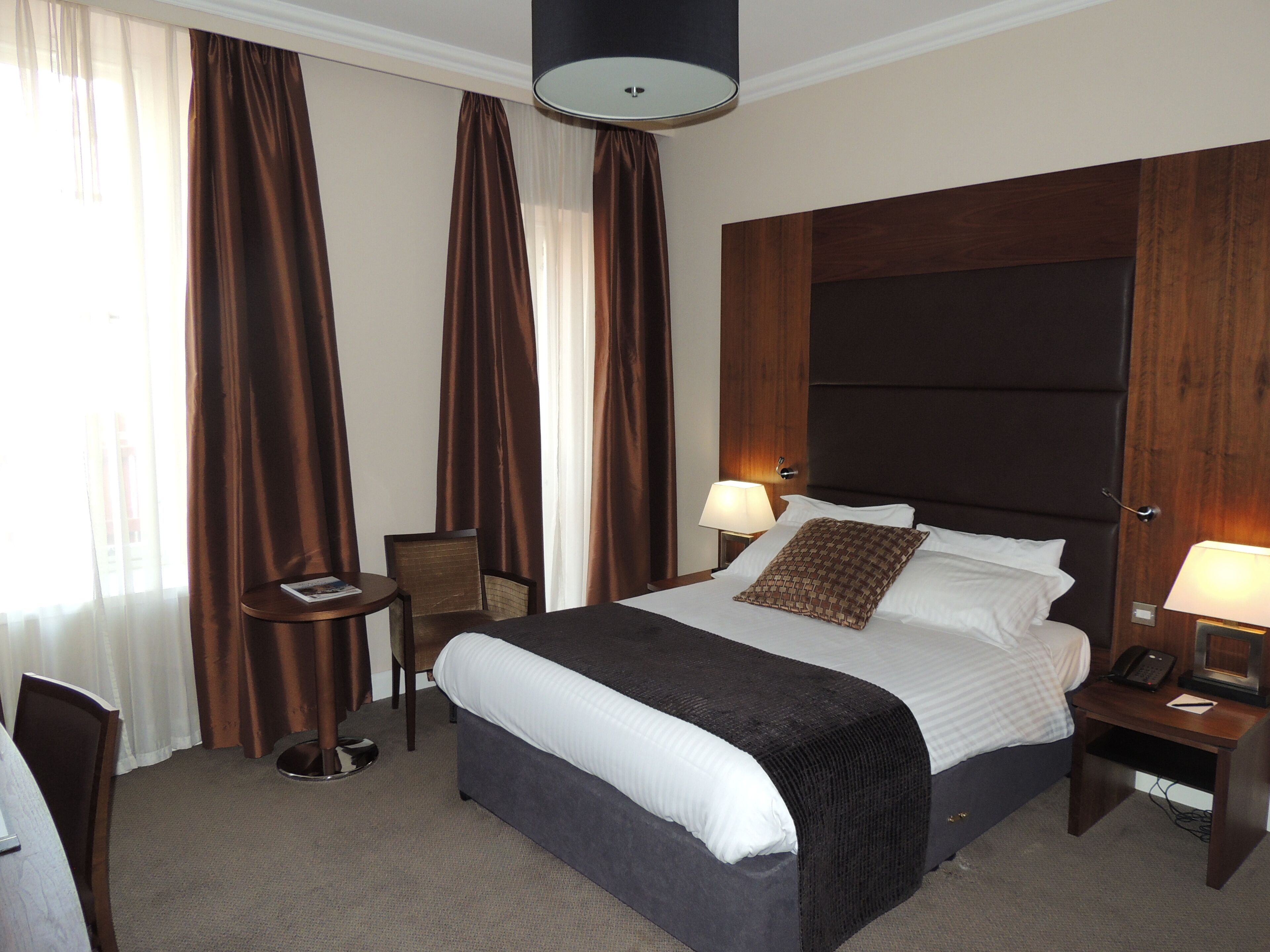 A hotel room with a large bed, two bedside tables with lamps, a chair, and a small table with a magazine.