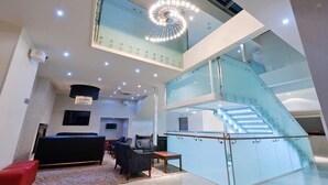 Un hall espacioso con una escalera moderna, una zona de estar y una lámpara de araña grande.