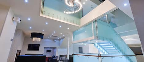 A spacious lobby with a modern staircase, seating area, and a large chandelier.