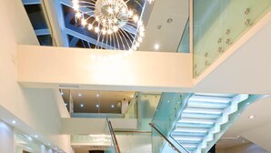 Un interior moderno con una escalera de cristal, un techo alto con una lámpara circular y vistas al piso superior.