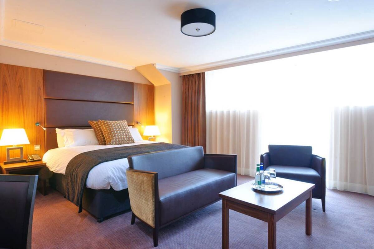A hotel room with a bed, two chairs, a table, and a nightstand.