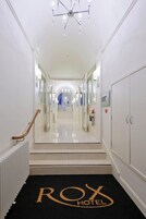 Un pasillo de hotel con alfombra negra que muestra el nombre del hotel, un candelabro y un extintor en la pared.