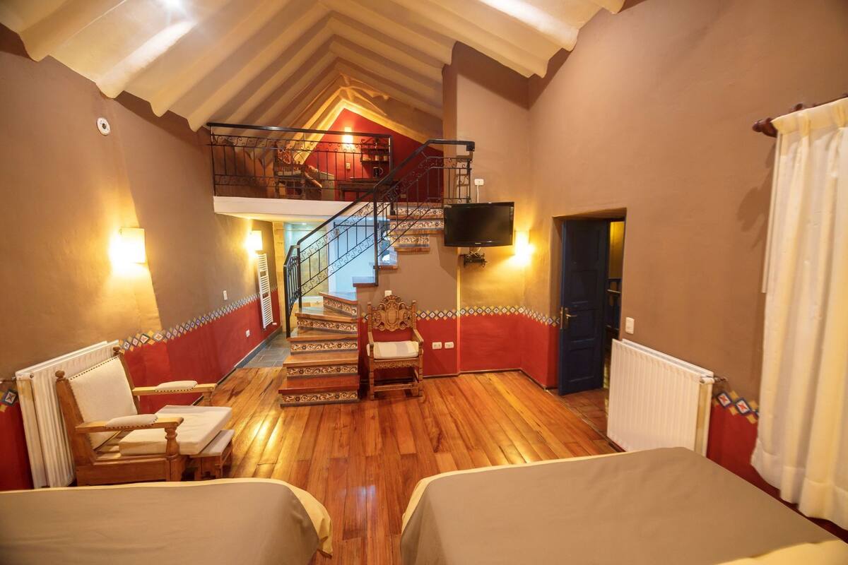Ein Zimmer mit Holzboden, einer Treppe, einem Bett, einem Stuhl, einem Fernseher und einer Tür.