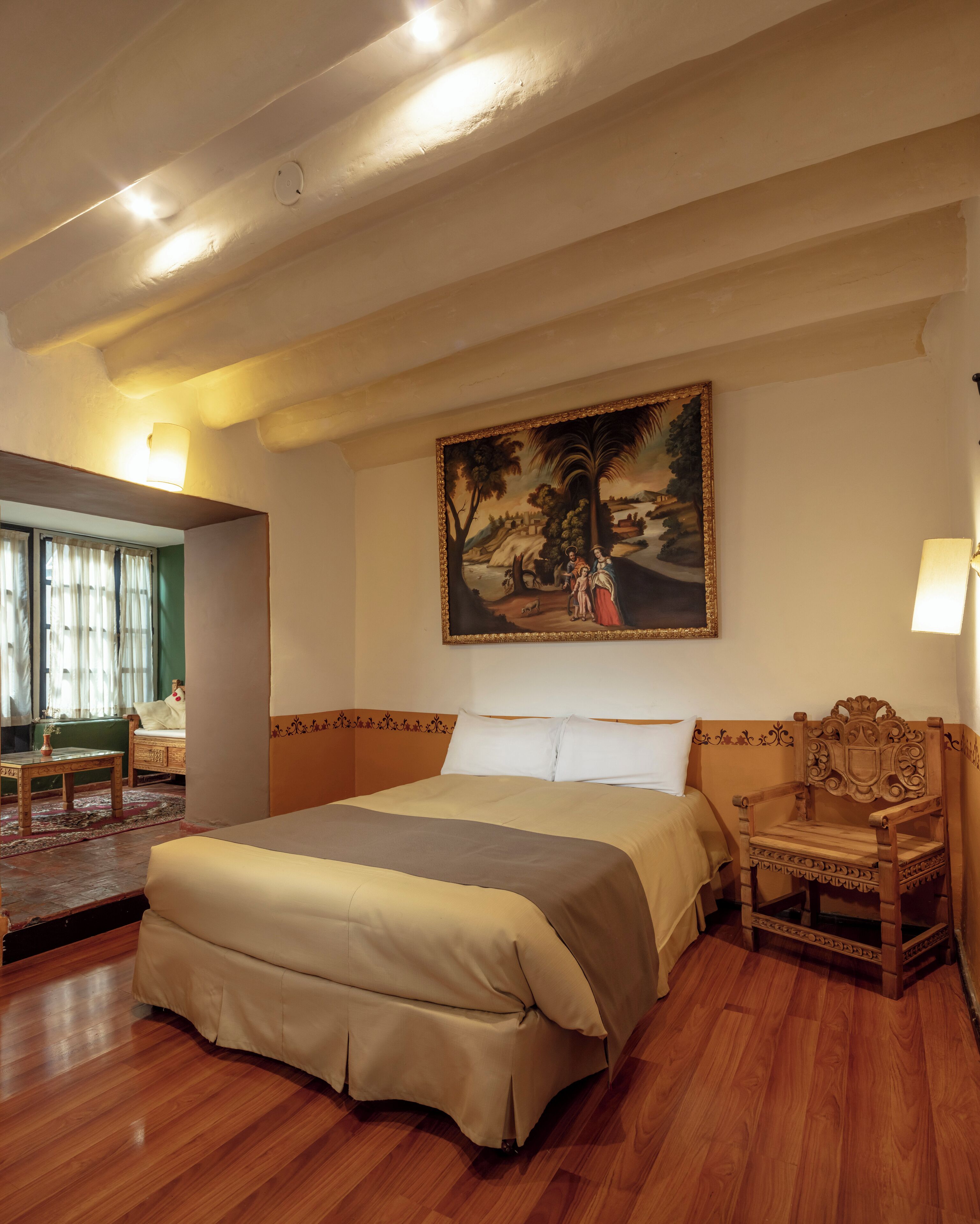 A bedroom with a large bed, a wooden chair, a painting on the wall, and a window with curtains.