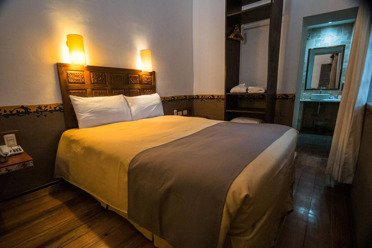 Ein Hotelzimmer mit Bett, Nachttischlampen, Telefon, Bad mit Spiegel und Dusche.