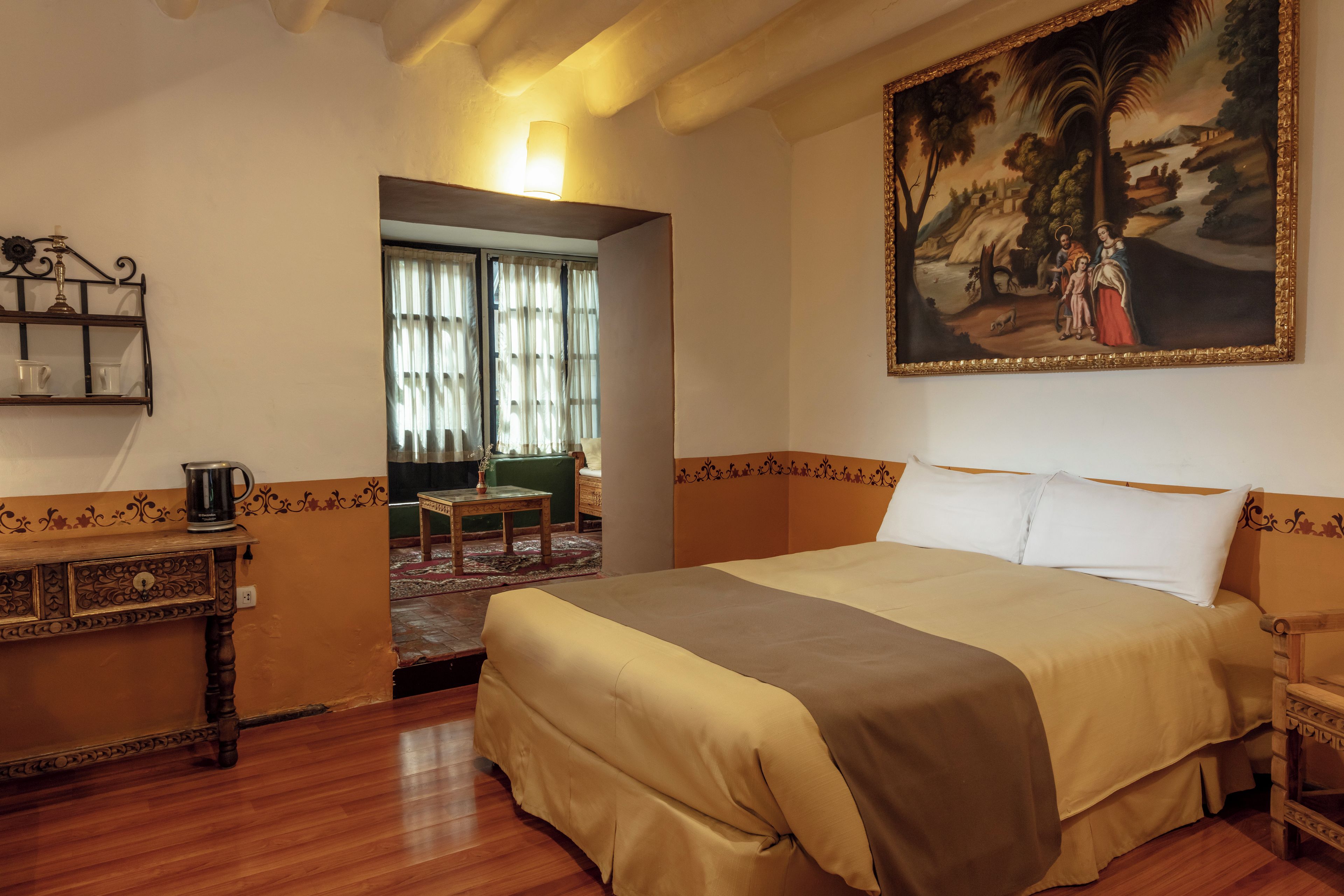 Een hotelkamer met een groot bed, een schilderij aan de muur, een tafeltje met een lamp en uitzicht naar buiten door een raam.