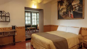 A hotel room with a large bed, a painting on the wall, a small table with a lamp, and a view of the outside through a window.