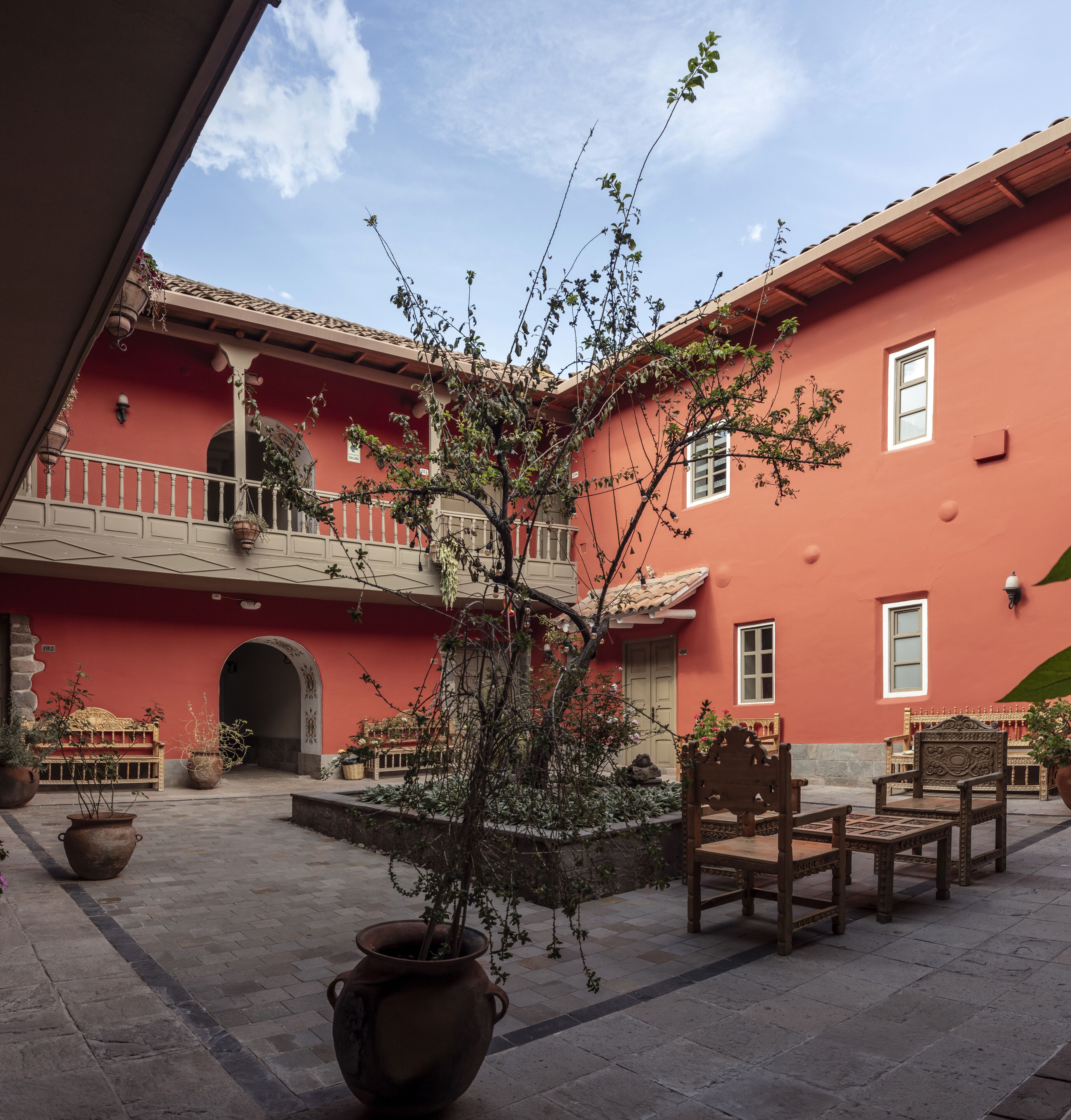 A courtyard with a red building, a wooden bench, a large pot, and a chair.