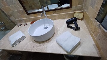 Casa de banho com uma grande pia branca, secador de cabelo portátil e duas toalhas dobradas no balcão.