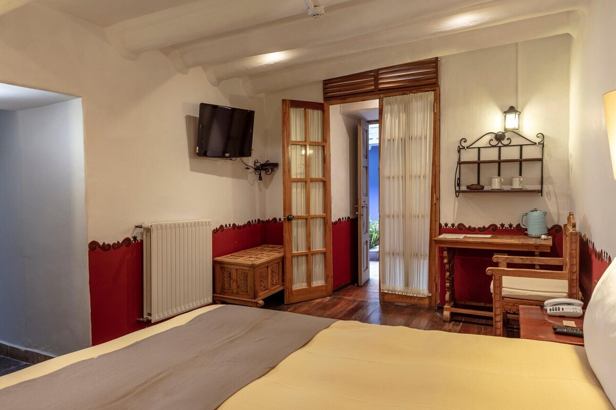 Een hotelkamer met een bed, een televisie, een houten kast, een tafel met waterkoker en een raam met gordijnen.