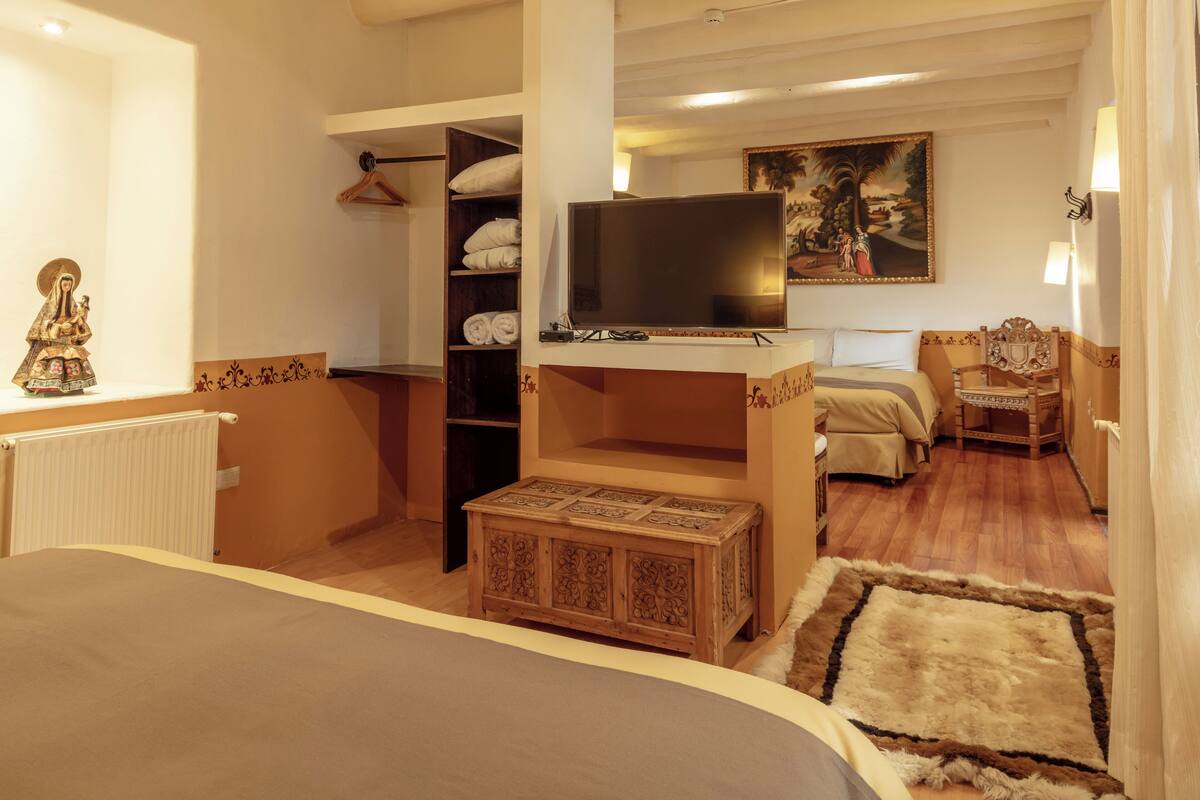 Ein Hotelzimmer mit einem großen Bett, einem Fernseher, einem Kleiderschrank, einem Gemälde an der Wand und einer kleinen Holzkabine.