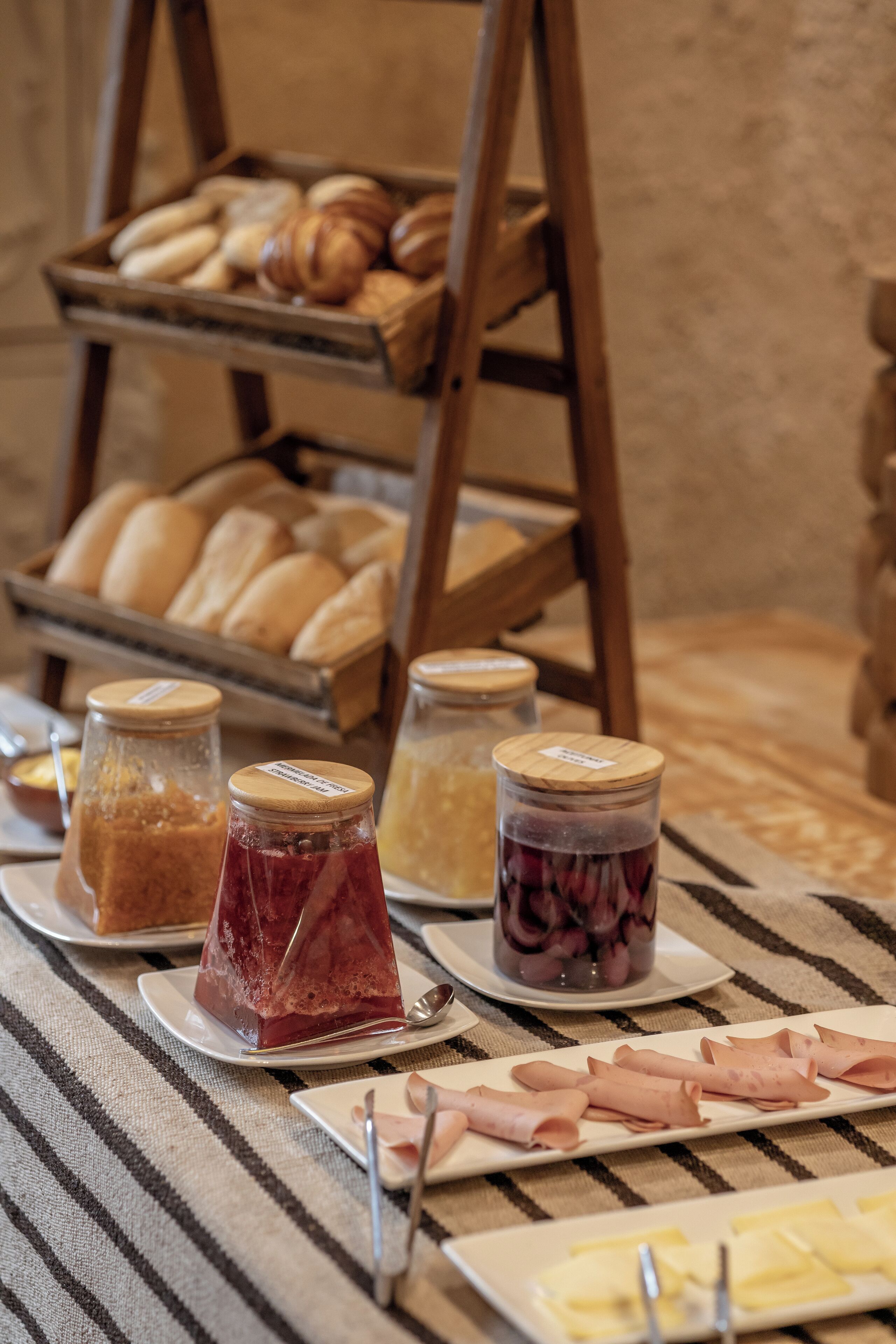 Una mesa de buffet con diversas opciones de comida, como pasteles, mermeladas y fiambres.