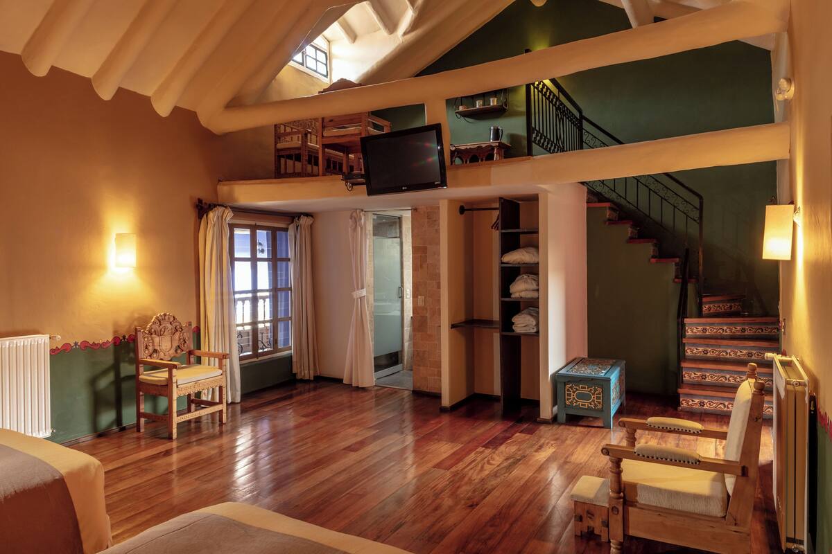 Ein geräumiges Schlafzimmer im Loft-Stil mit Holzboden, einem großen Fenster, einem eingebauten Fernseher und einer Treppe zu einer erhöhten Ebene.