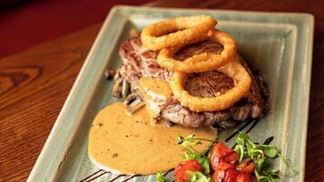 A square plate with a steak, onion rings, a creamy sauce, and a side of greens.