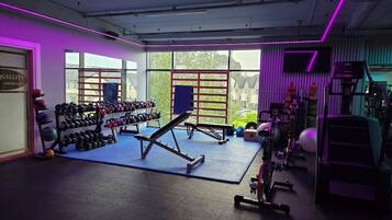 A gym with exercise equipment, large windows, and a view of greenery.