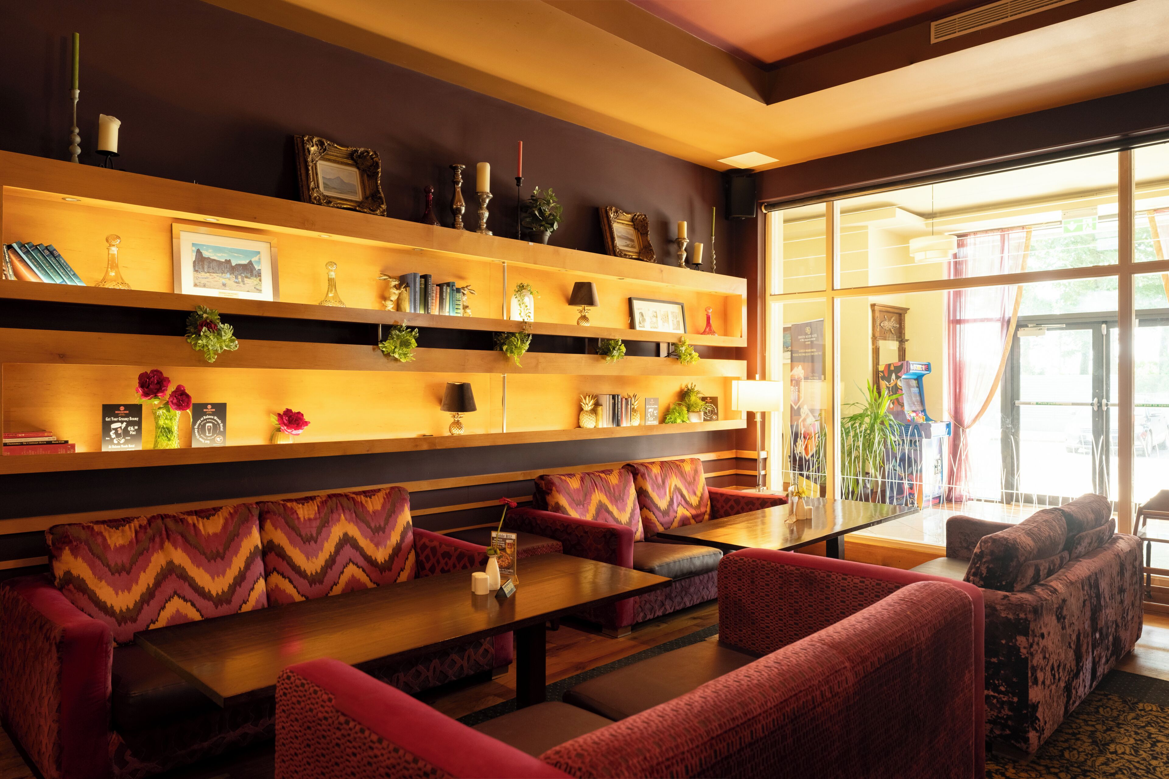 A hotel lobby with a wooden reception desk, seating area with patterned cushions, and a large window with a view of the outdoors.