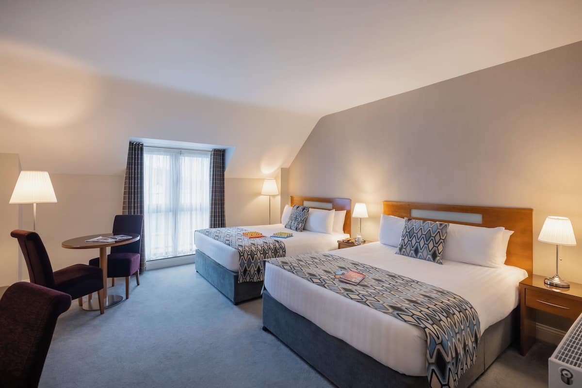 Une chambre d’hôtel avec deux lits, un bureau, une chaise et une fenêtre avec des rideaux.