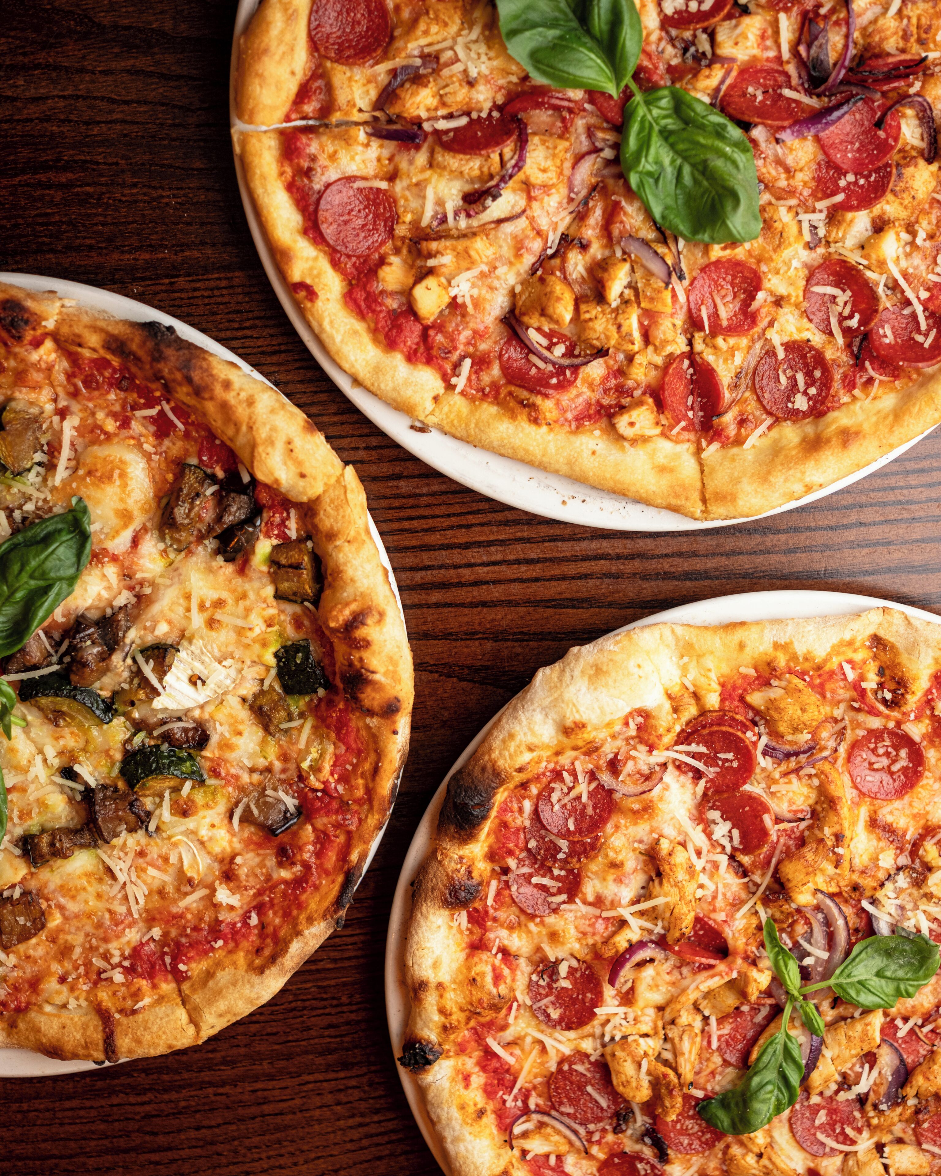 Tre pizzor med olika sorters toppingar på ett träbord.