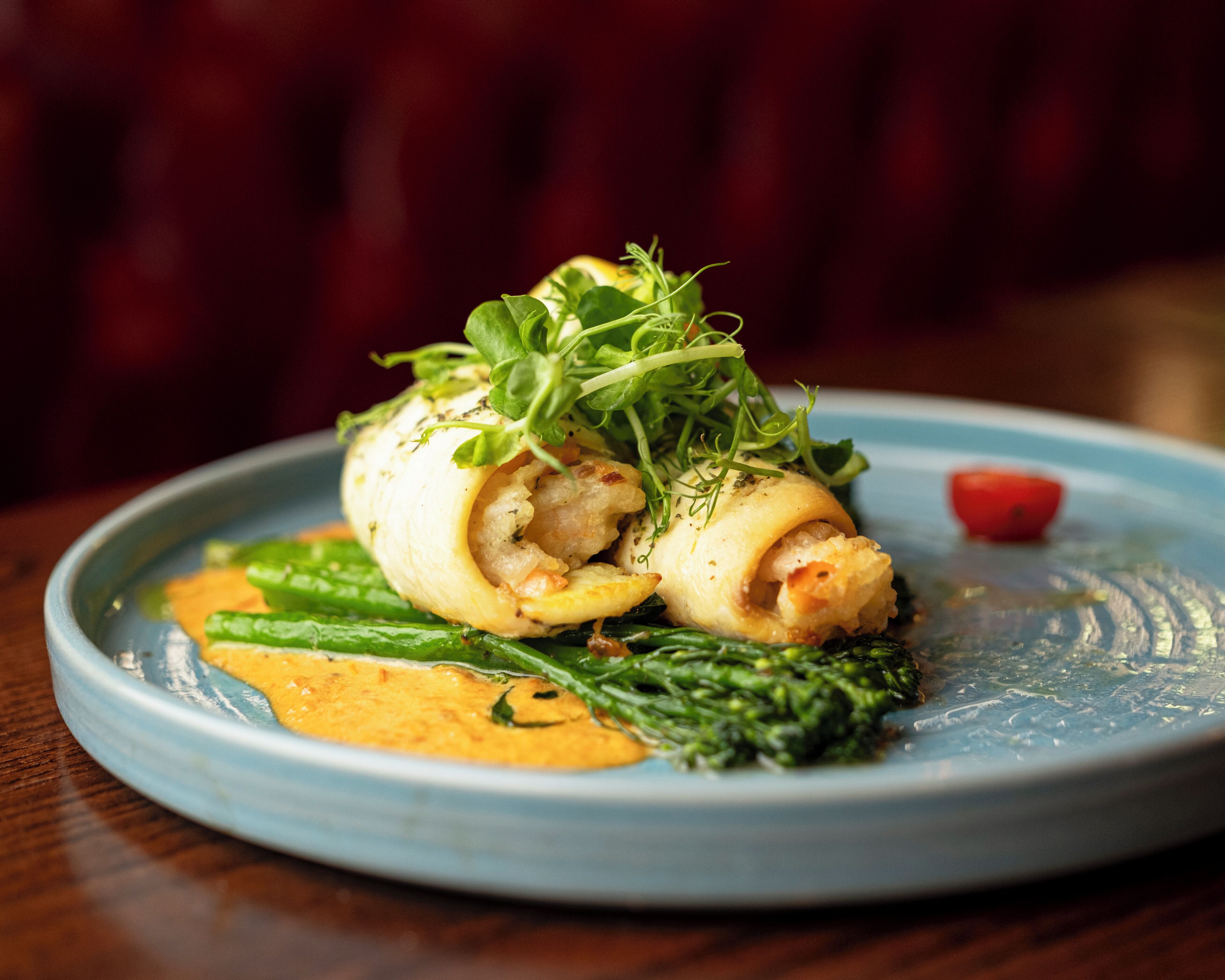 A plate with a rolled dish, greens, and a small tomato.