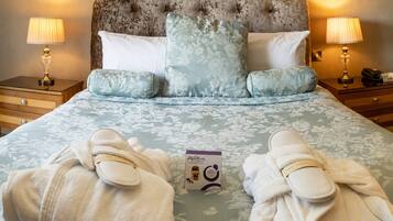 A hotel room with a tufted headboard, floral-patterned bedding, two bedside lamps, a nightstand with a phone, and a box of toiletries.