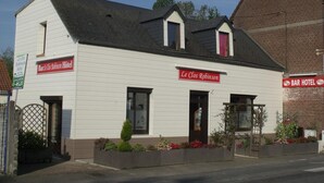 Ein zweistöckiges Gebäude mit weißer Fassade und schwarzem Dach, mit Hinweisschildern für 'Bar Le Clos Robinson Hôtel' und 'Le Clos Robinson'.