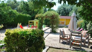 Ein Patio mit Holzterrasse, Gartenmöbeln und einer kleinen Spielanlage.
