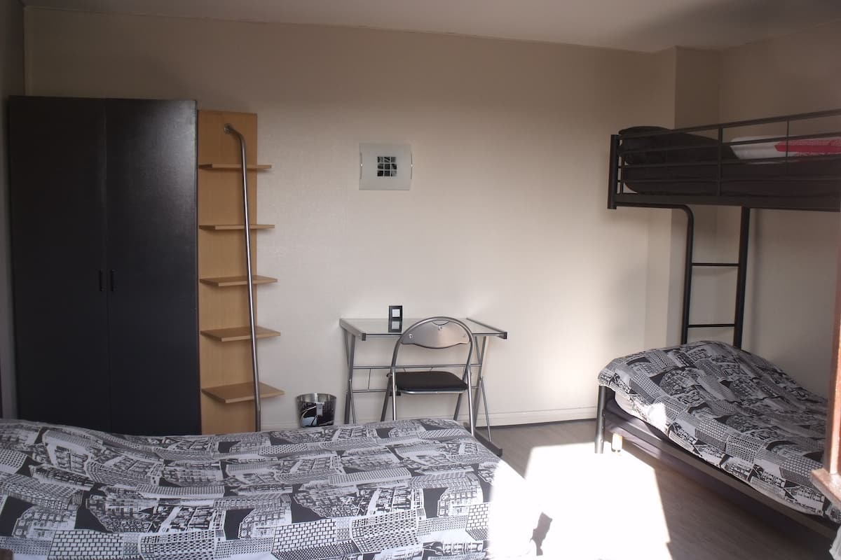 A dormitory room with bunk beds, a desk, a chair, and a wardrobe.
