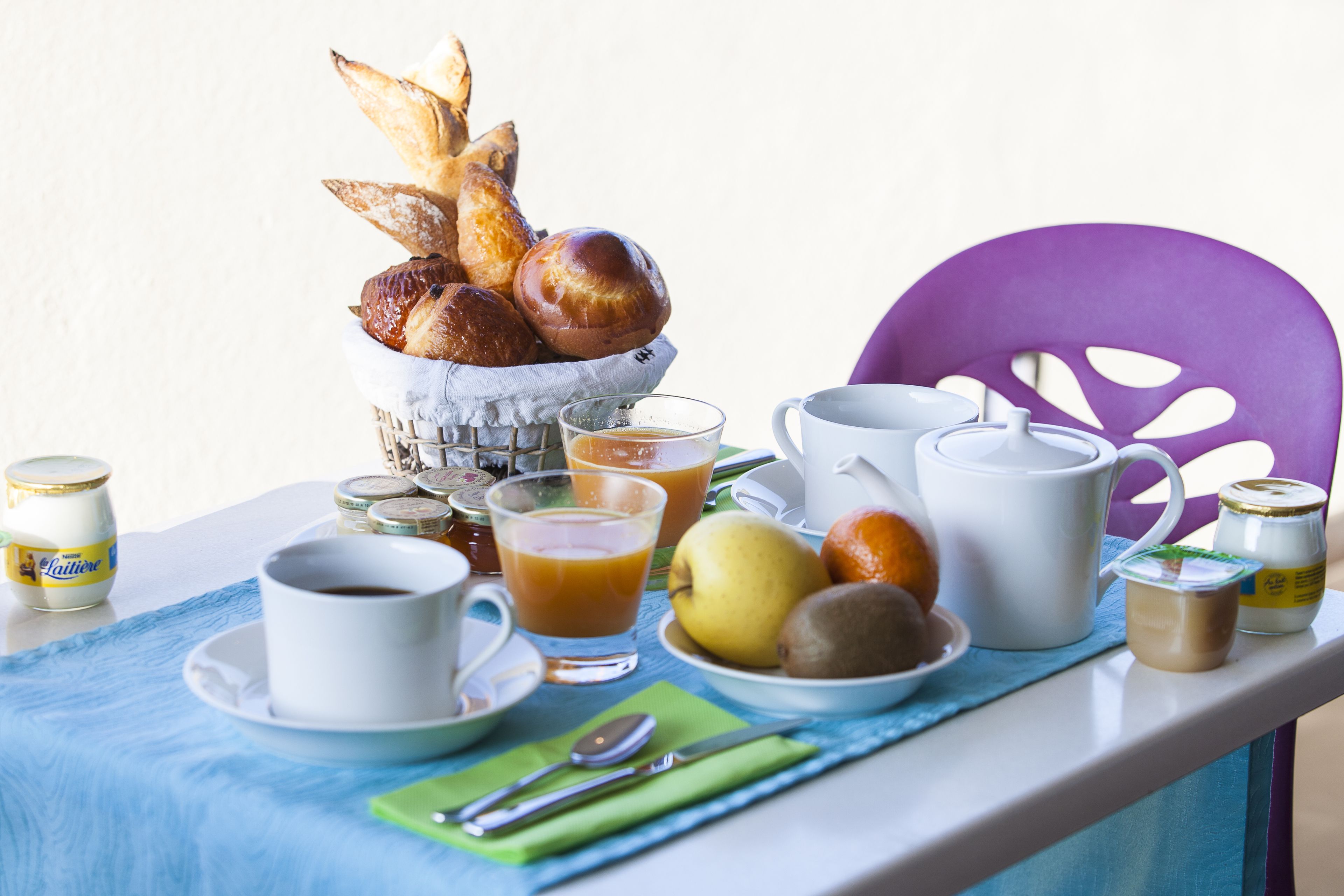 A breakfast setup with bread, fruits, coffee, and tea on a table.