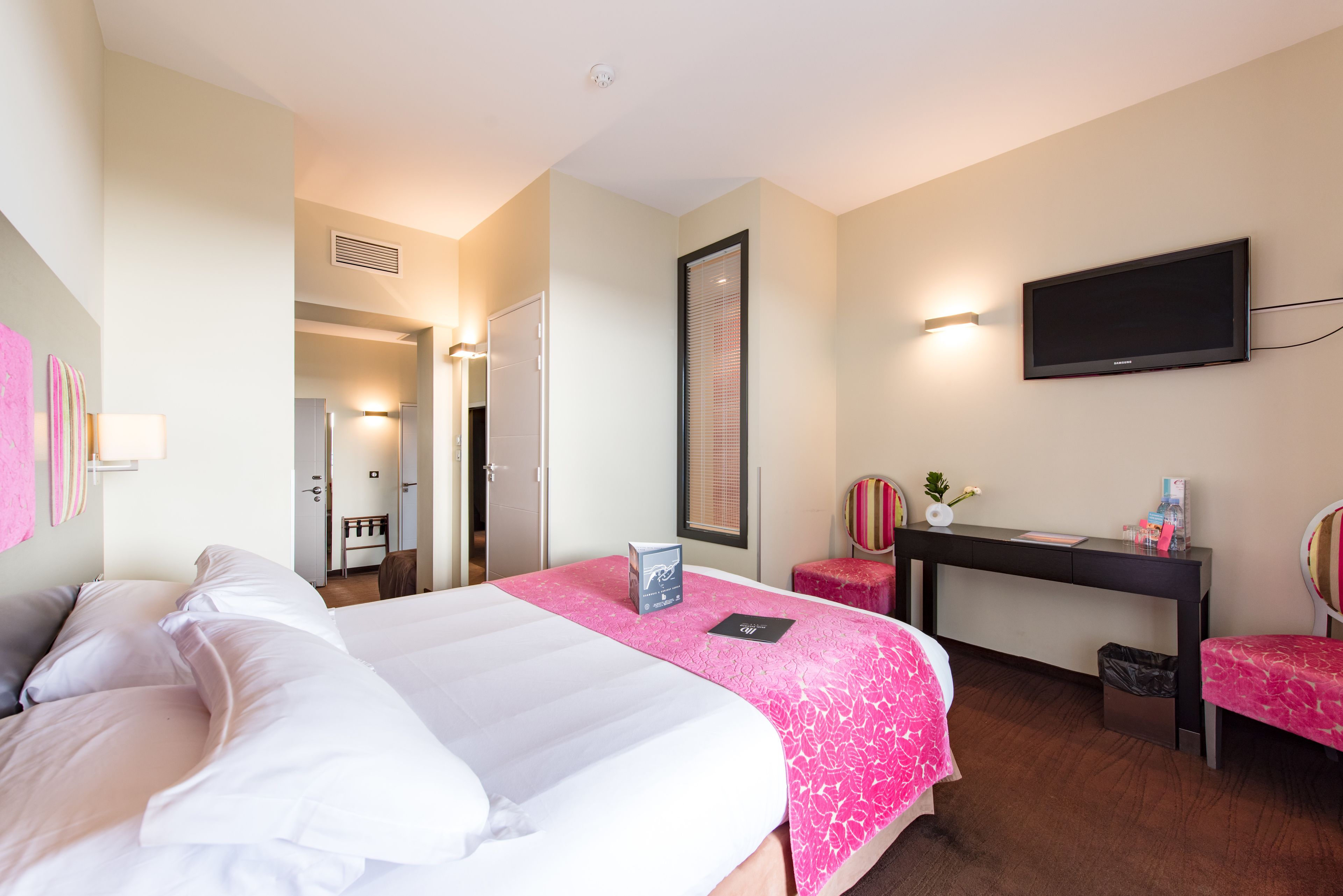 A hotel room with a large bed, a desk, a chair, a TV, and a trash bin.