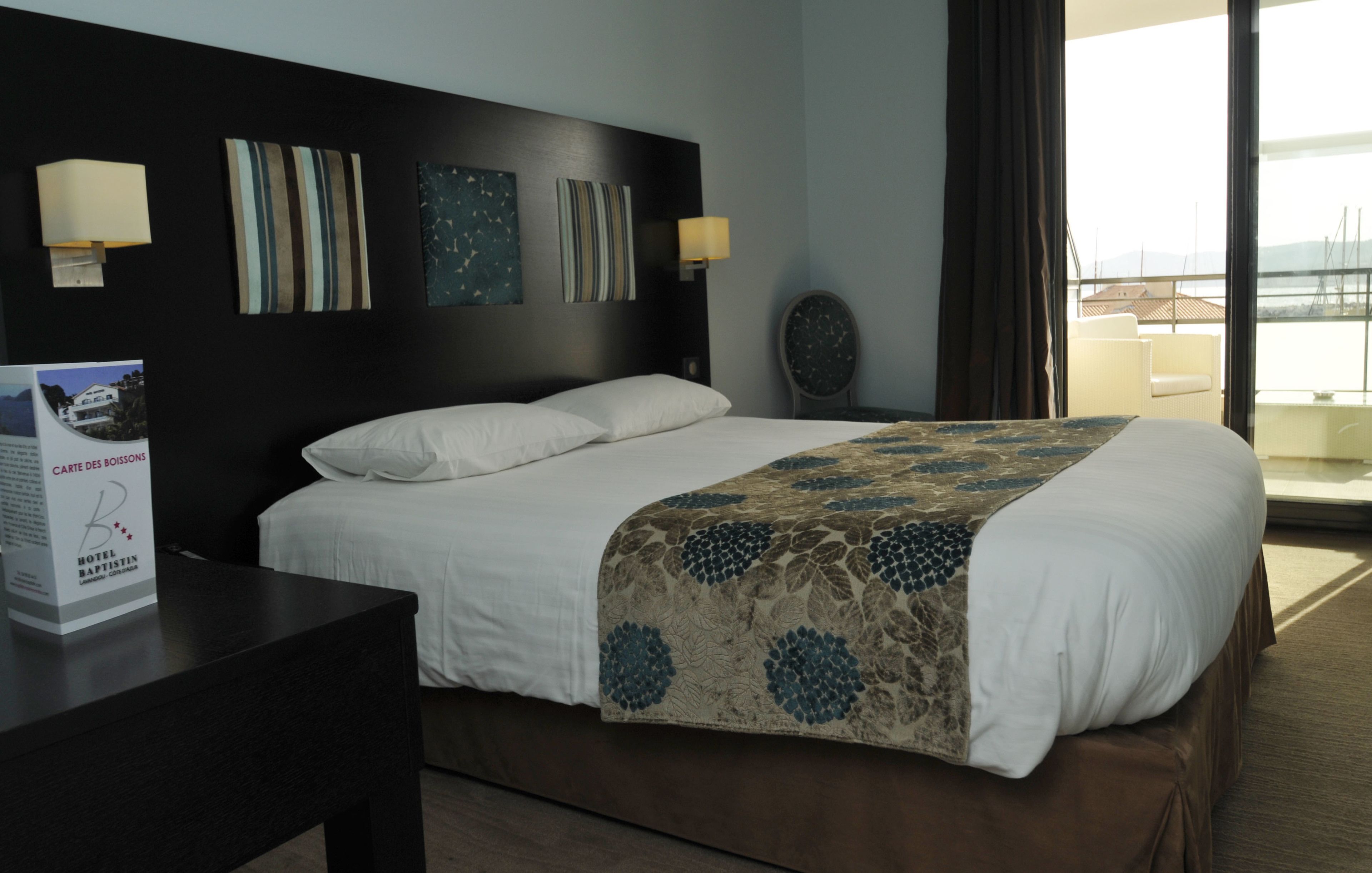 Una camera d'albergo con un letto grande, un comodino, una lampada a parete e vista mare dalla finestra.