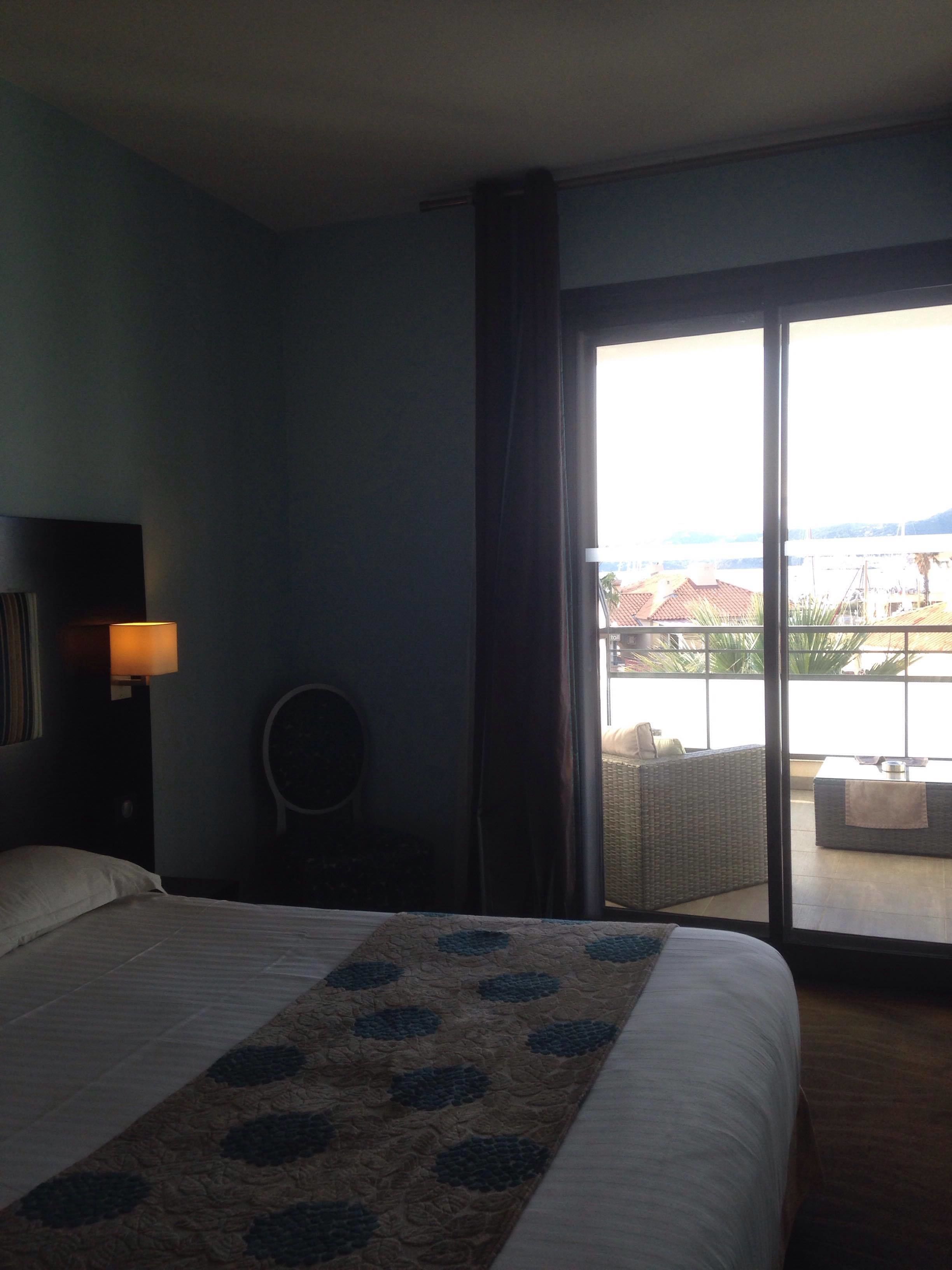 Ein Hotelzimmer mit Bett, einem Sessel, einer Lampe und Blick ins Freie.