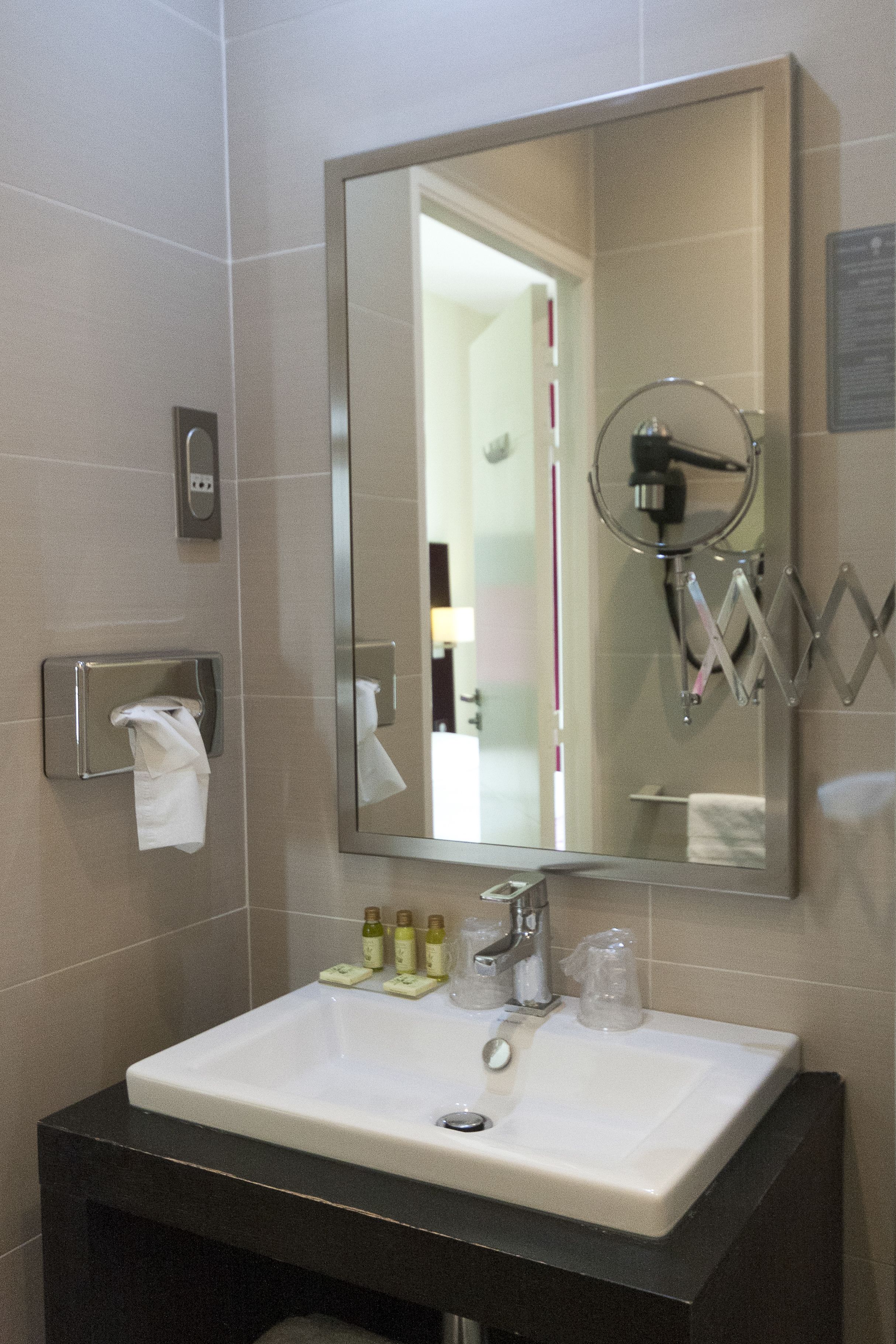 Une salle de bain équipée d’un lavabo, d’un miroir, d’un distributeur de serviettes et d’articles de toilette.