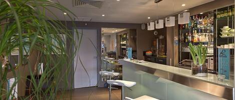 A modern bar area with a counter, stools, and a variety of bottles and glasses.