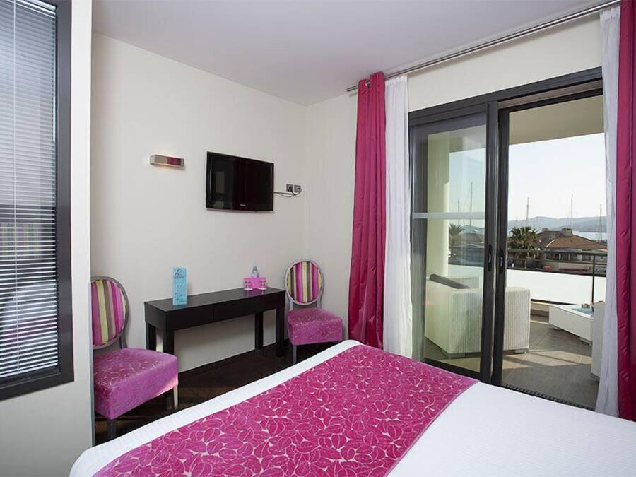 A hotel room with a bed, a desk, two chairs, a TV, and a balcony with a view.